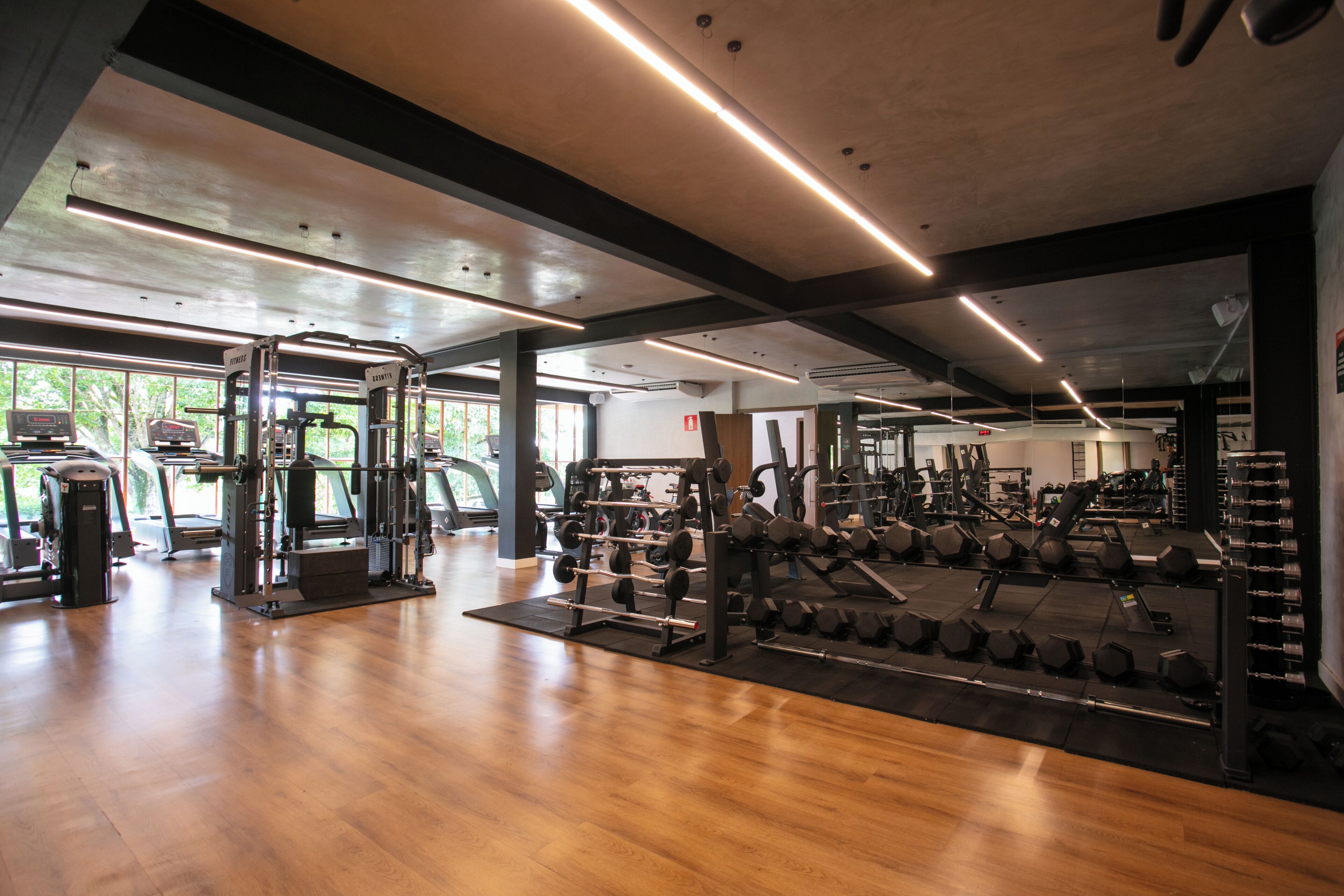 A gym with various exercise equipment, wooden flooring, and large windows allowing natural light.