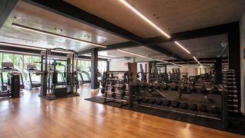 A gym with various exercise equipment, wooden flooring, and large windows allowing natural light.