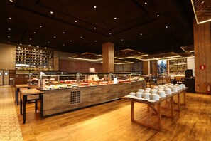 A buffet setup with multiple serving stations, a long counter with stacked plates, and a variety of food items. - Tauá Resort Caeté (Caete)