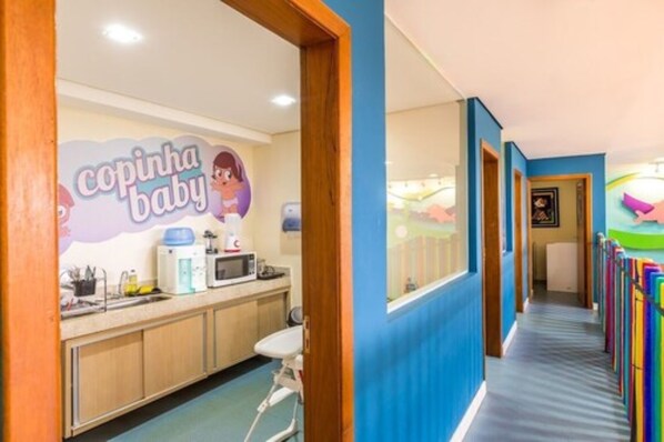 Un espace de jeux pour enfants aux couleurs vives, avec une enseigne « Copinha Baby », un parc à jeux et une fresque murale colorée.