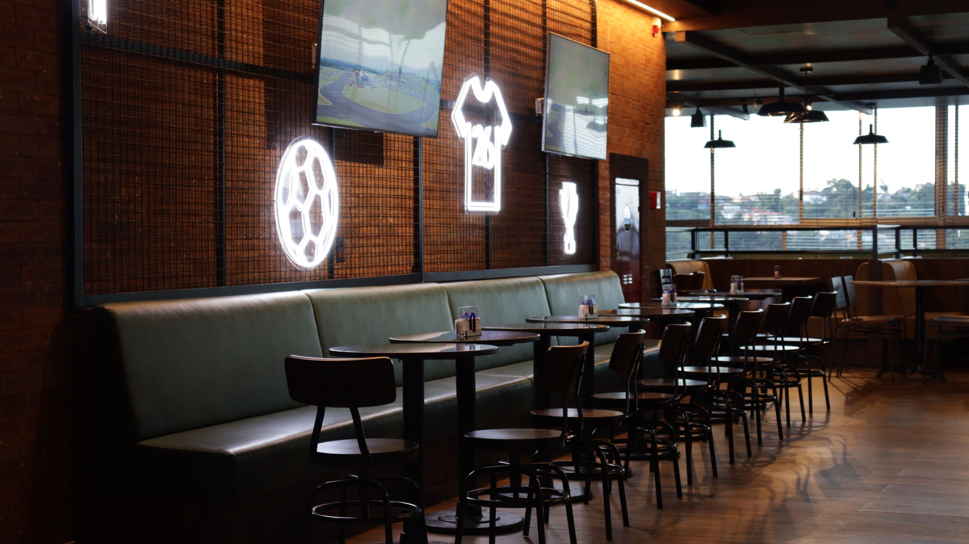 Interior de restaurante con una barra alargada, cabinas y una pared de ladrillo con iconos deportivos iluminados.
