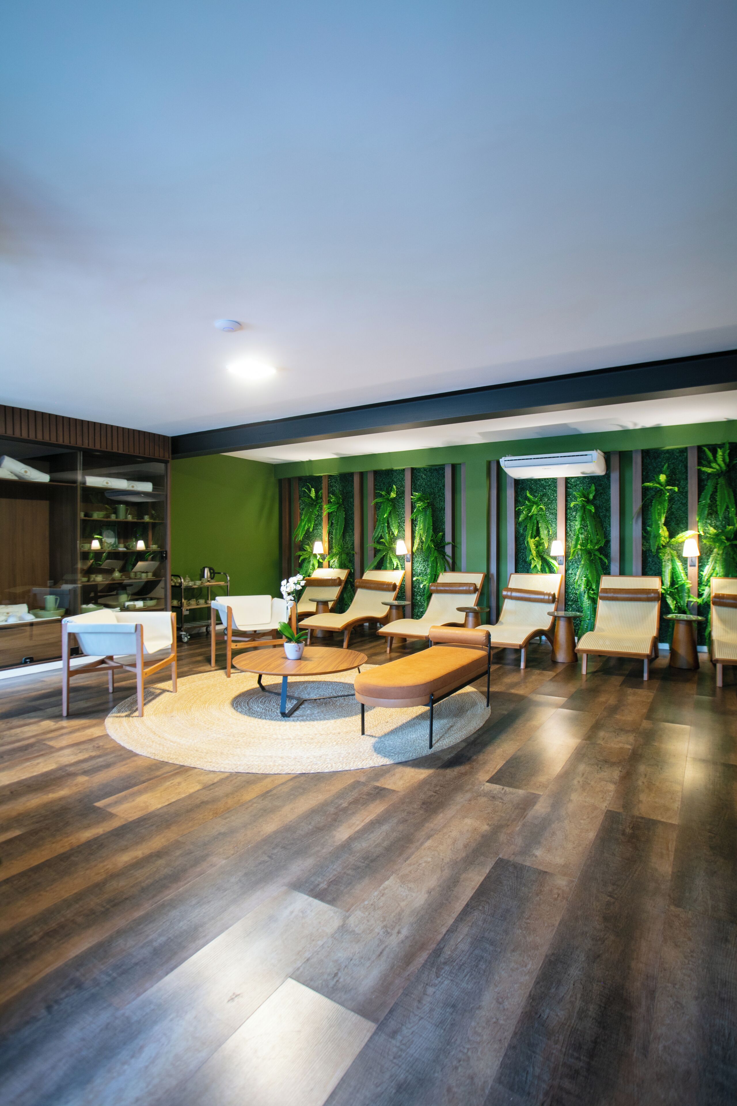 Un área de lounge moderna con asientos, una mesa de centro y una pared verde con plantas.