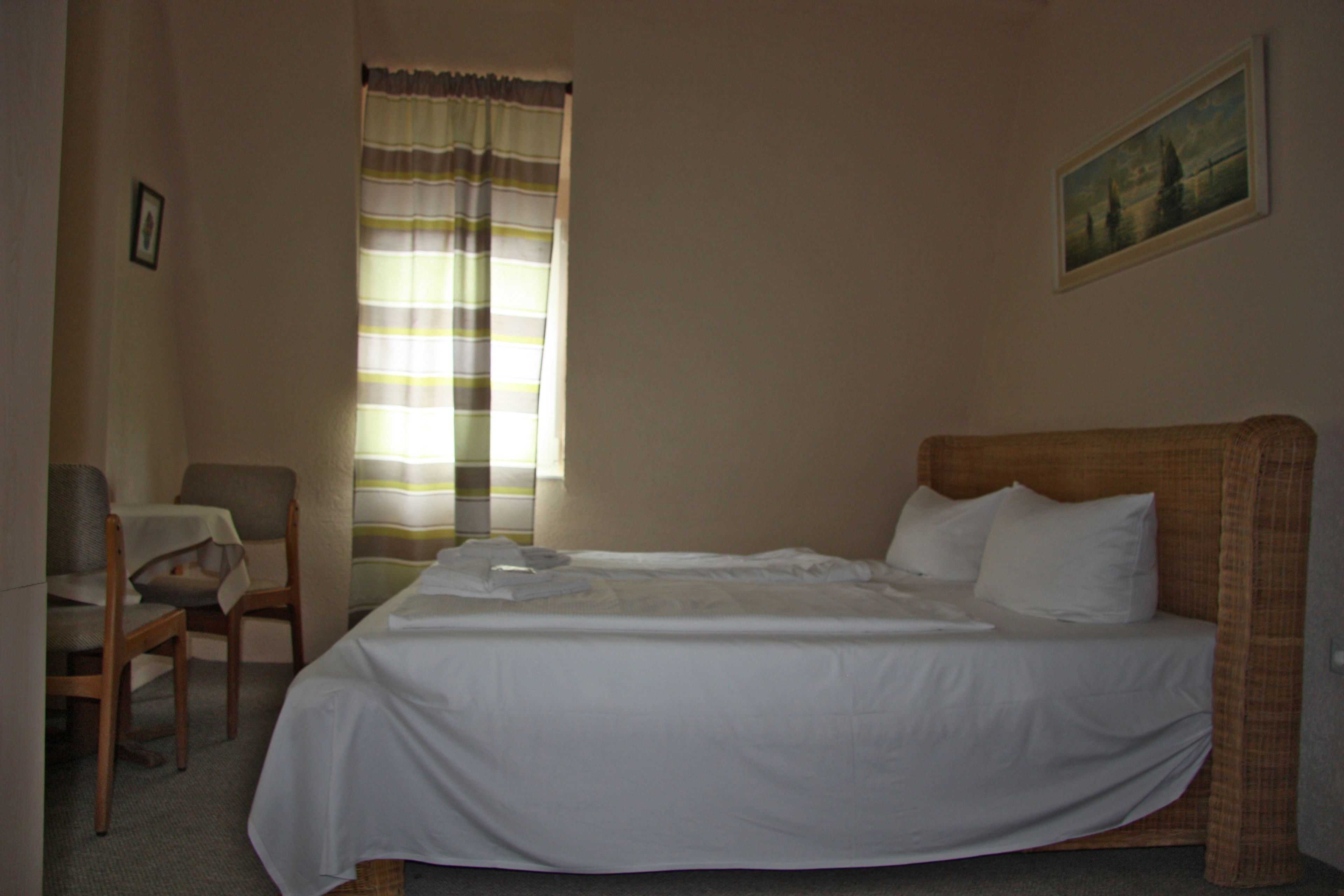 A hotel room with a single bed, a chair, a table, and a window with curtains.