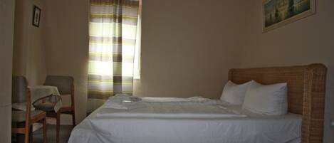 A hotel room with a single bed, a chair, a table, and a window with curtains.