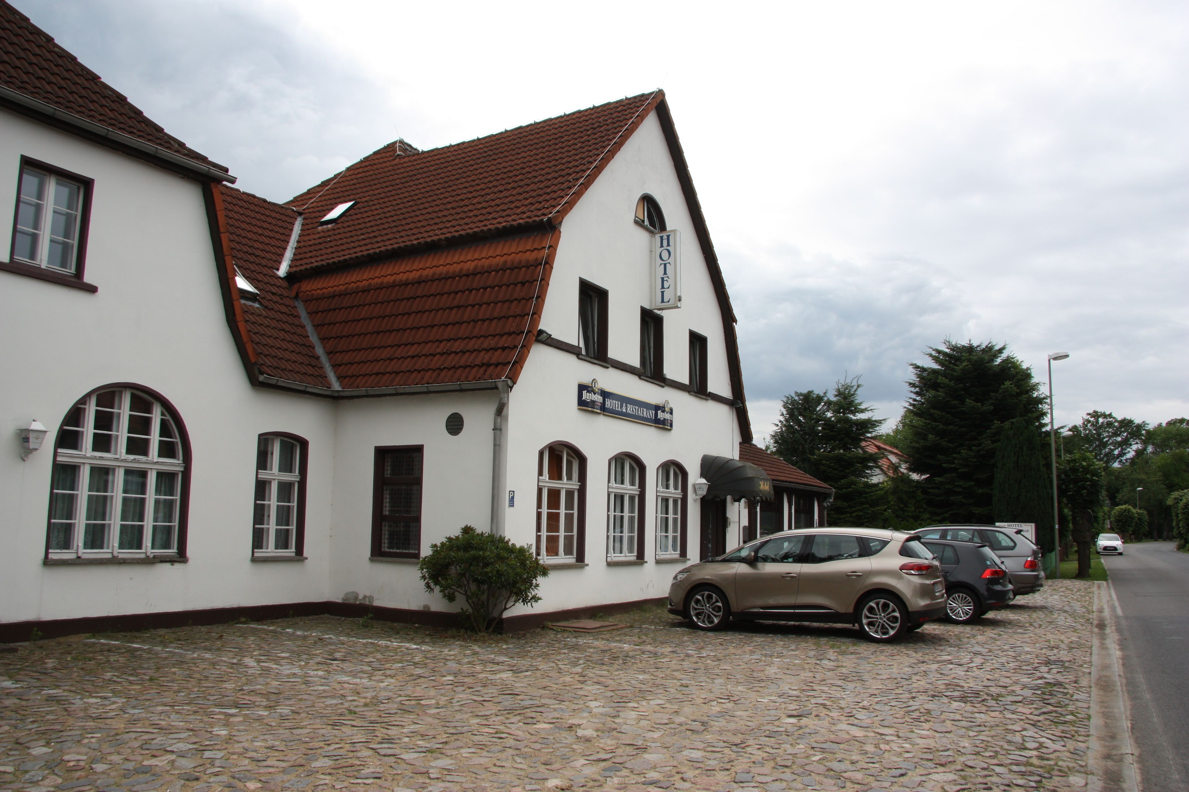 A white building with a brown roof, a sign reading "HOTEL & RESTAURANT," and a cobblestone ground.
