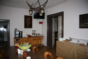 A dining area with a wooden table, chairs, a buffet table, a television mounted on the wall, and a kitchen area with appliances. - Hotel - Zum goldenen Stern (Unterspreewald)