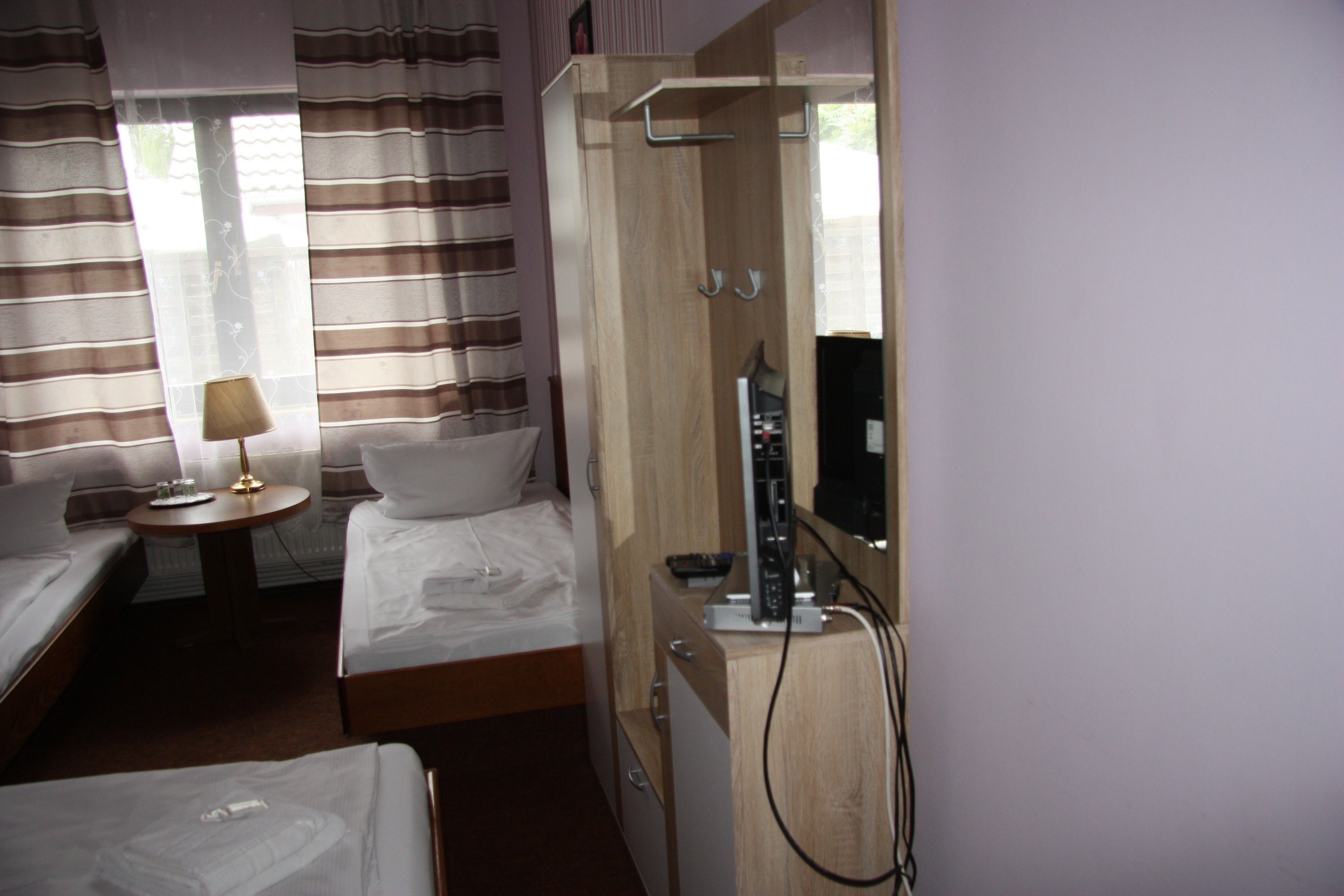 A hotel room with two single beds, a small bedside table with a lamp, a wardrobe, and a mirror.