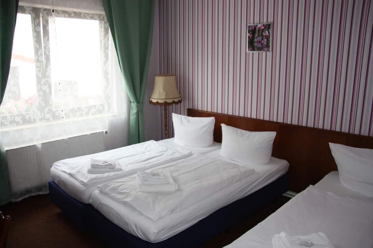 A hotel room with a neatly made bed, a bedside lamp, and a window with curtains.