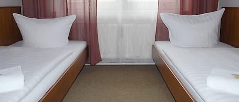 Een hotelkamer met twee enkele bedden, een houten hoofdeinde, een vloerbedekking en lichte gordijnen.