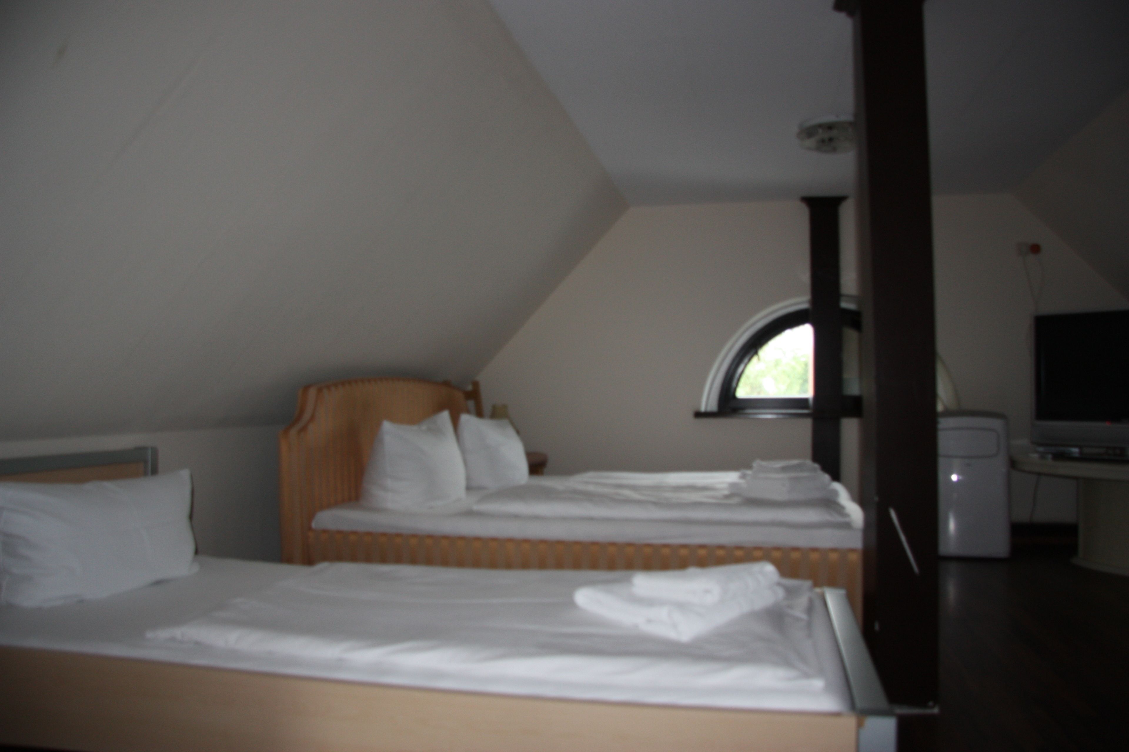 A bedroom with two beds, a window, and a desk with a television.