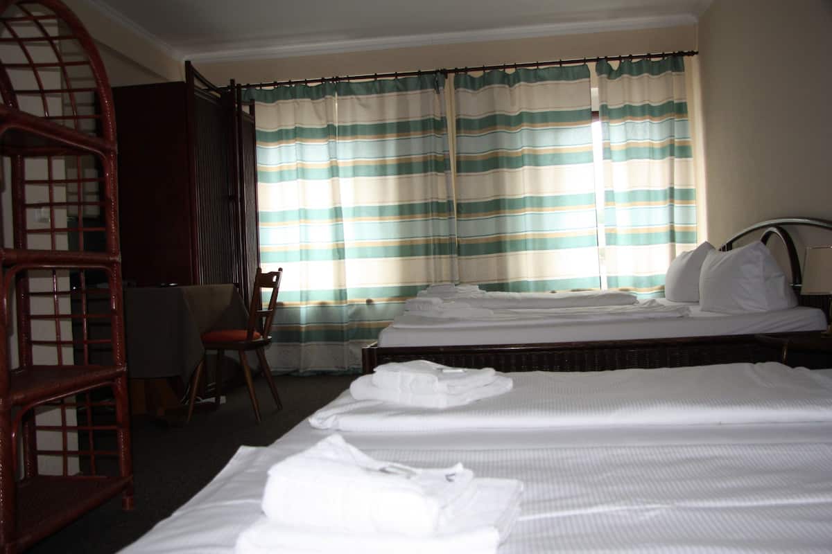 A hotel room with two beds, a chair, and a wooden chair with a lattice backrest.