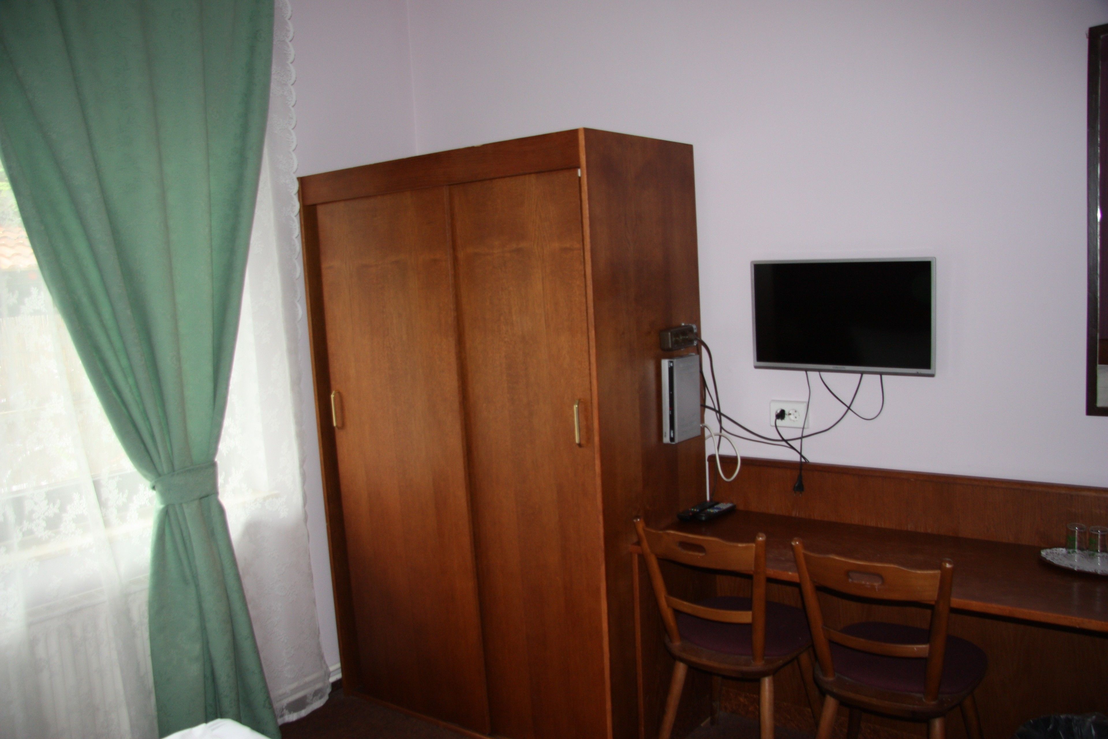 Ein Zimmer mit einem Holfischschrank, einem Schreibtisch mit zwei Stühlen und einem an der Wand befestigten Fernseher.