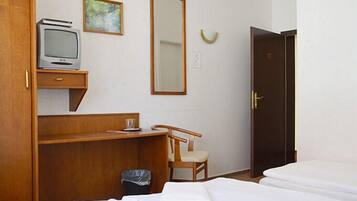 A hotel room with a bed, a desk with a television, a chair, a mirror, and a door.