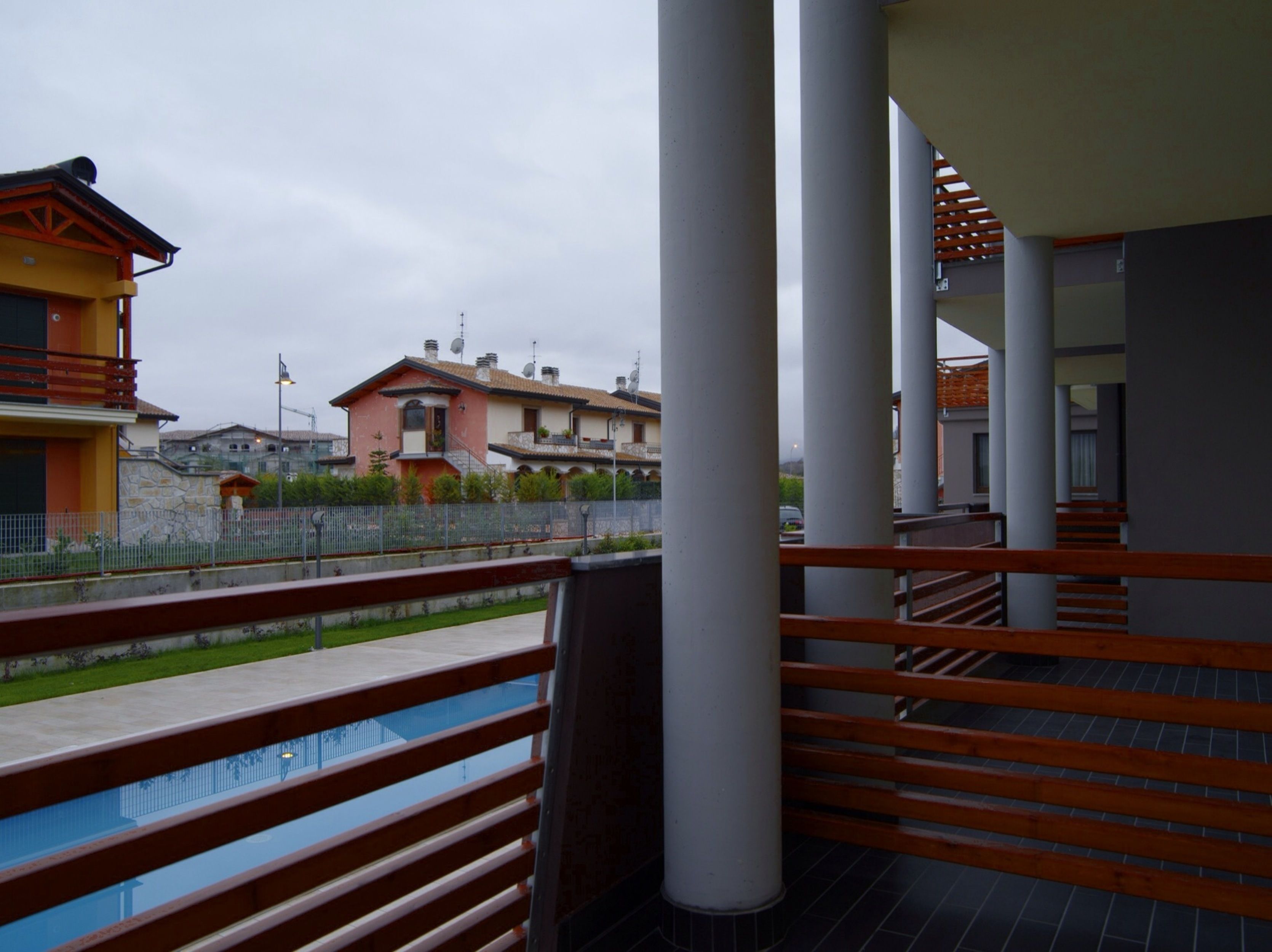 Ein Balkon mit Pool, weißen Säulen und Blick auf Wohnhäuser.