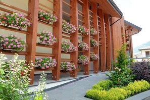 Um edifício com várias colunas de madeira que sustentam uma varanda com jardineiras floridas.