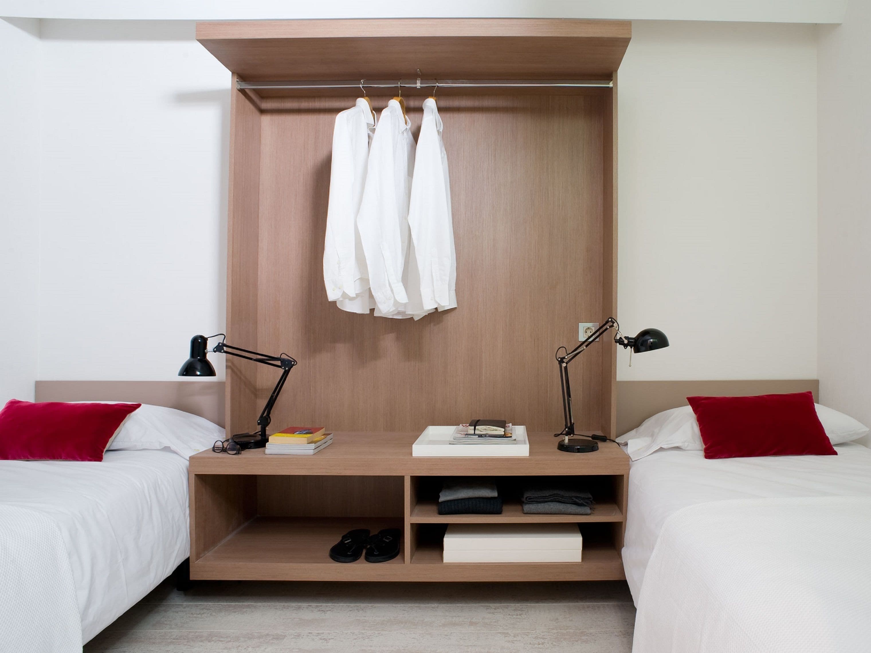 Habitació d'hotel moderna amb dos llits, un armari de fusta i escriptori amb una làmpada.