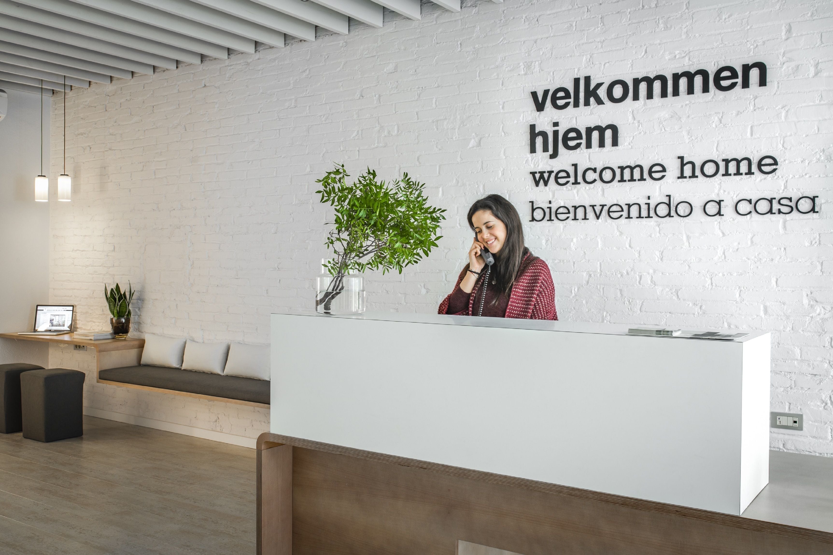 A reception area with a white brick wall, a reception desk, a seating area with a bench, and a potted plant.
