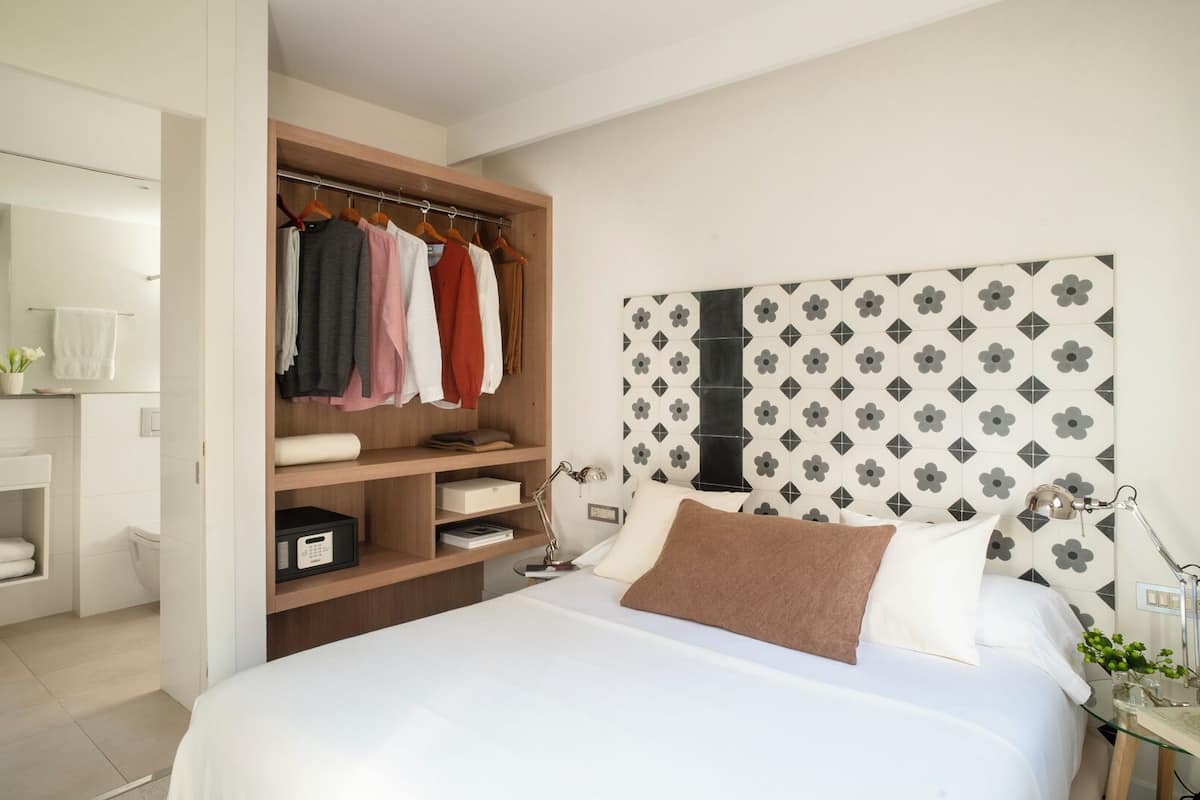 A bedroom with a bed, bedside table, lamp, and a built-in wardrobe with hanging clothes.