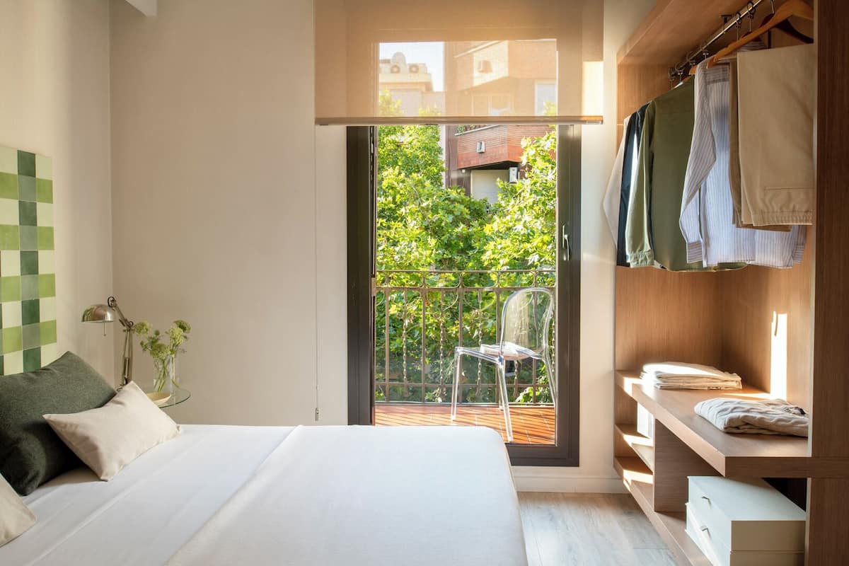 A bedroom with a bed, a nightstand, a wardrobe, and a balcony with a chair.