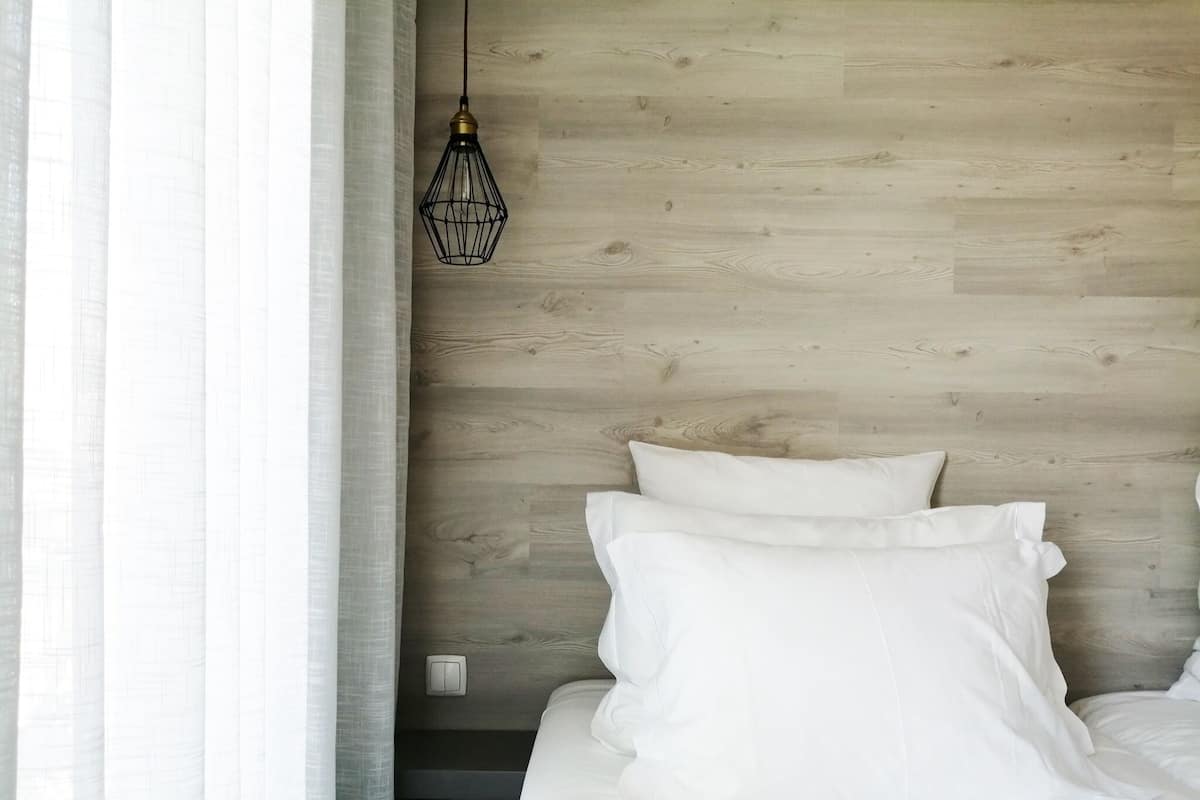 A bedroom with a wooden headboard, white bedding, and a hanging light fixture.