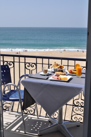 A balcony with a table set for breakfast overlooking a beach. - Hotel Mar Bravo (Nazaré)