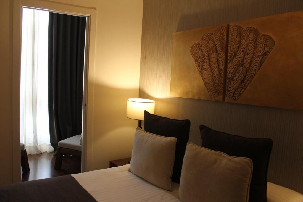 A hotel room with a bed, two pillows, a nightstand with a lamp, a chair, and a large abstract painting on the wall.