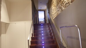 A staircase with wooden steps and a handrail, leading to a landing with a stone wall and a door at the top.