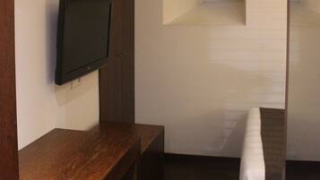 Una habitación moderna con una televisión de pantalla plana montada en un mueble de madera, una ventana pequeña y una cama con colchón blanco.