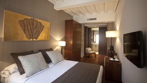 A hotel room with a large bed, two bedside lamps, a TV, and a painting on the wall.