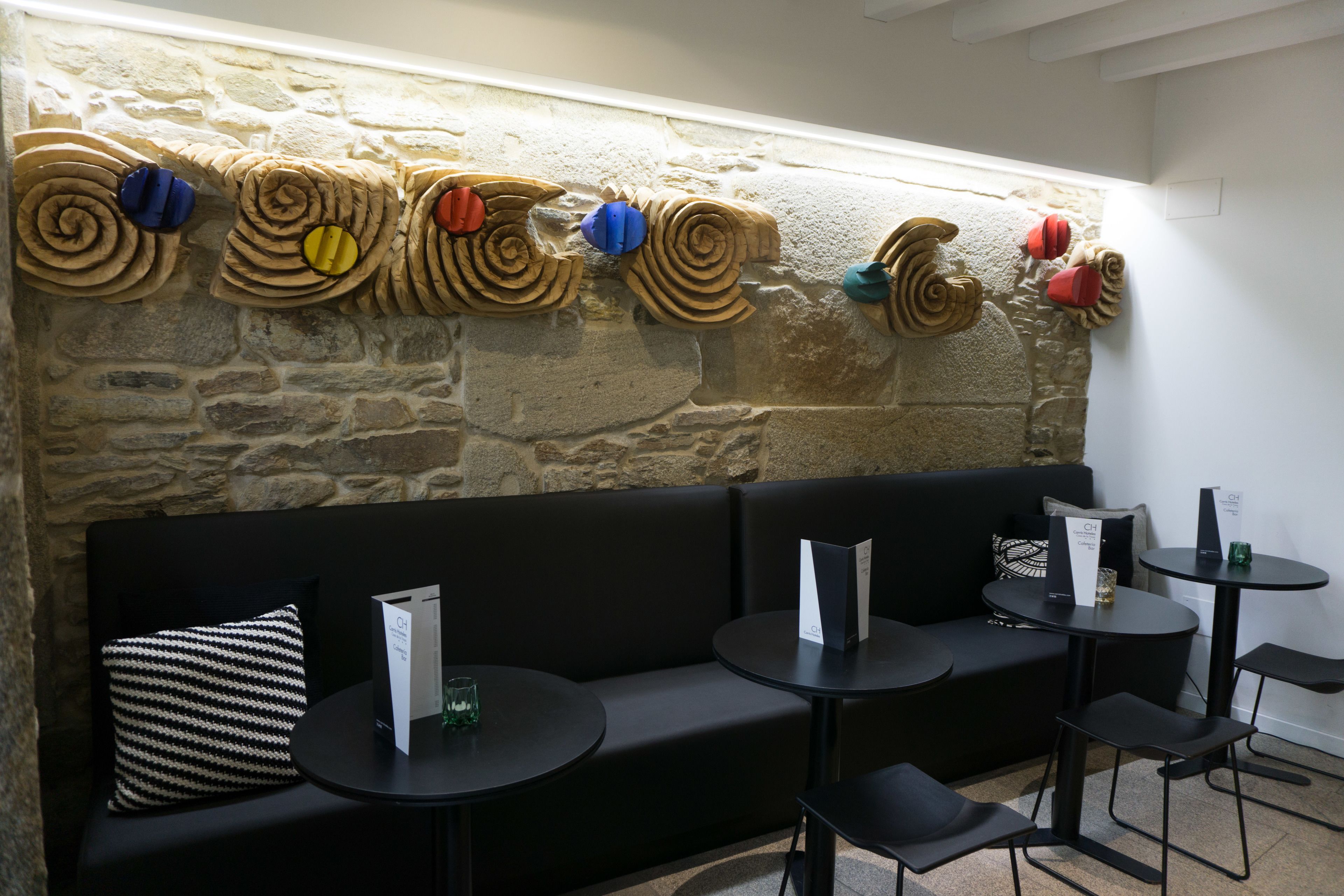 Een modern interieur met een stenen muur, zwarte bekleding en ronde tafels.