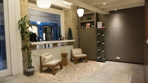 A reception area with a stone wall, a reception desk, two chairs, a potted plant, a chandelier, and a wine refrigerator.