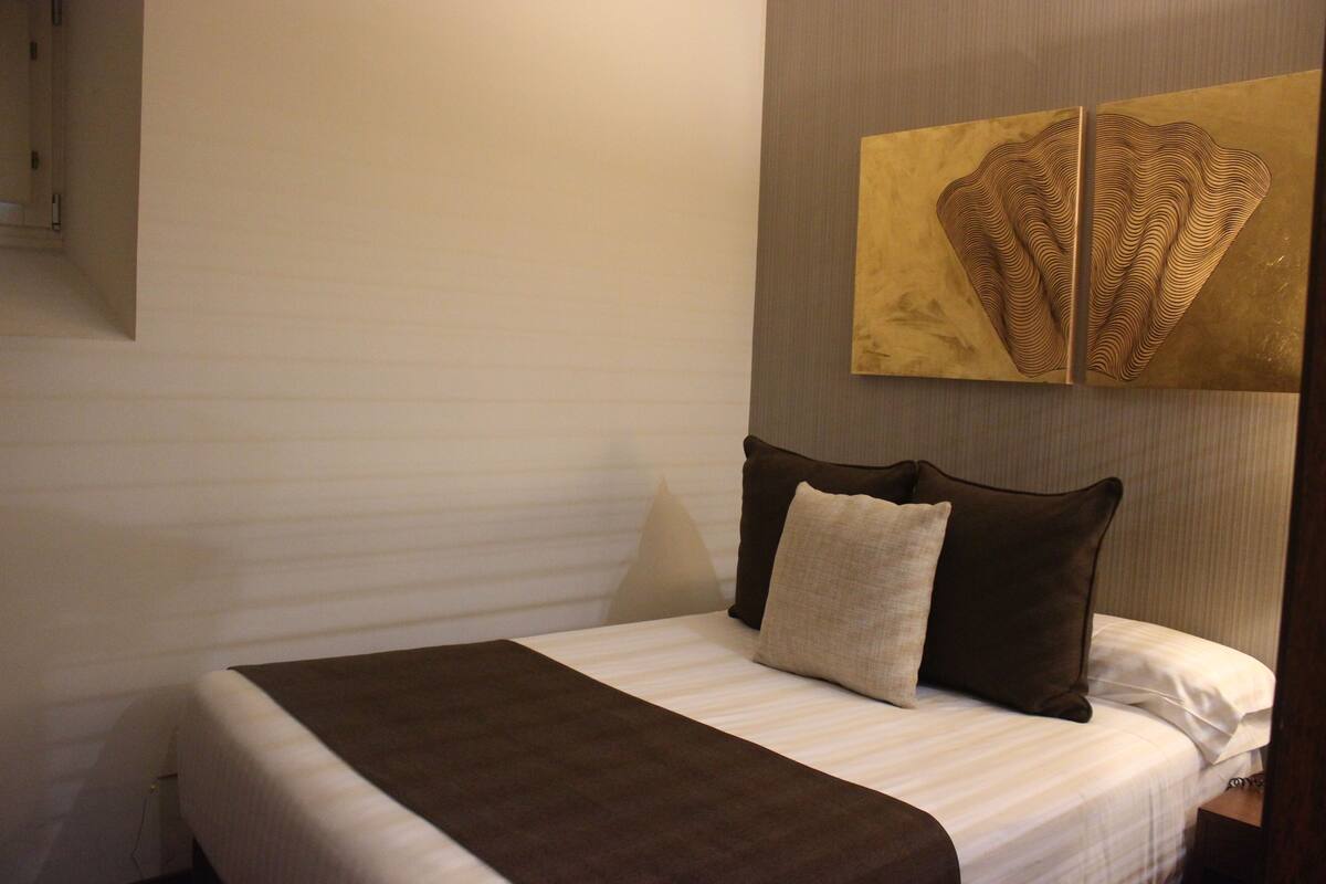 A hotel room with a bed, pillows, a wall-mounted artwork, and a nightstand.