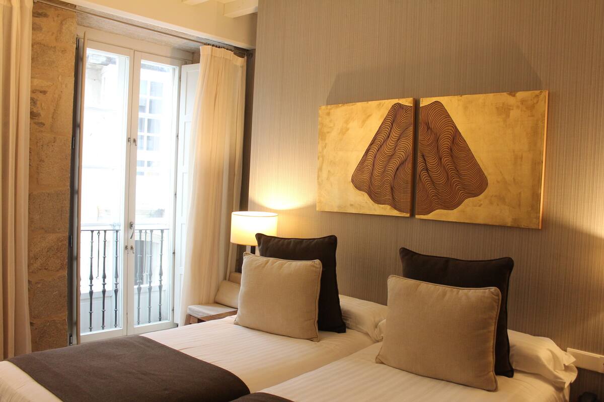 A hotel room with a bed, a nightstand, a lamp, a painting, and a balcony with curtains.