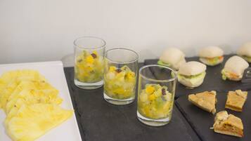 A table with sliced pineapple, three glasses of fruit punch, and several sandwiches.