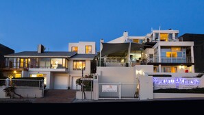 A modern multi-story hotel with a well-lit entrance and a visible guest house. - BlaauwVillage Boutique Guest House (Cape Town)