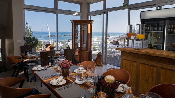 A restaurant with a view of the ocean, wooden furniture, and a bar area. - BlaauwVillage Boutique Guest House (Cape Town)