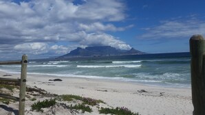 A beach with a wooden post in the foreground, waves crashing onto the shore, and a mountain in the background. - BlaauwVillage Boutique Guest House (Cape Town)