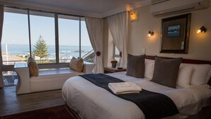 A bedroom with a large bed, a sofa, a view of the sea, and a framed picture on the wall. - BlaauwVillage Boutique Guest House (Cape Town)