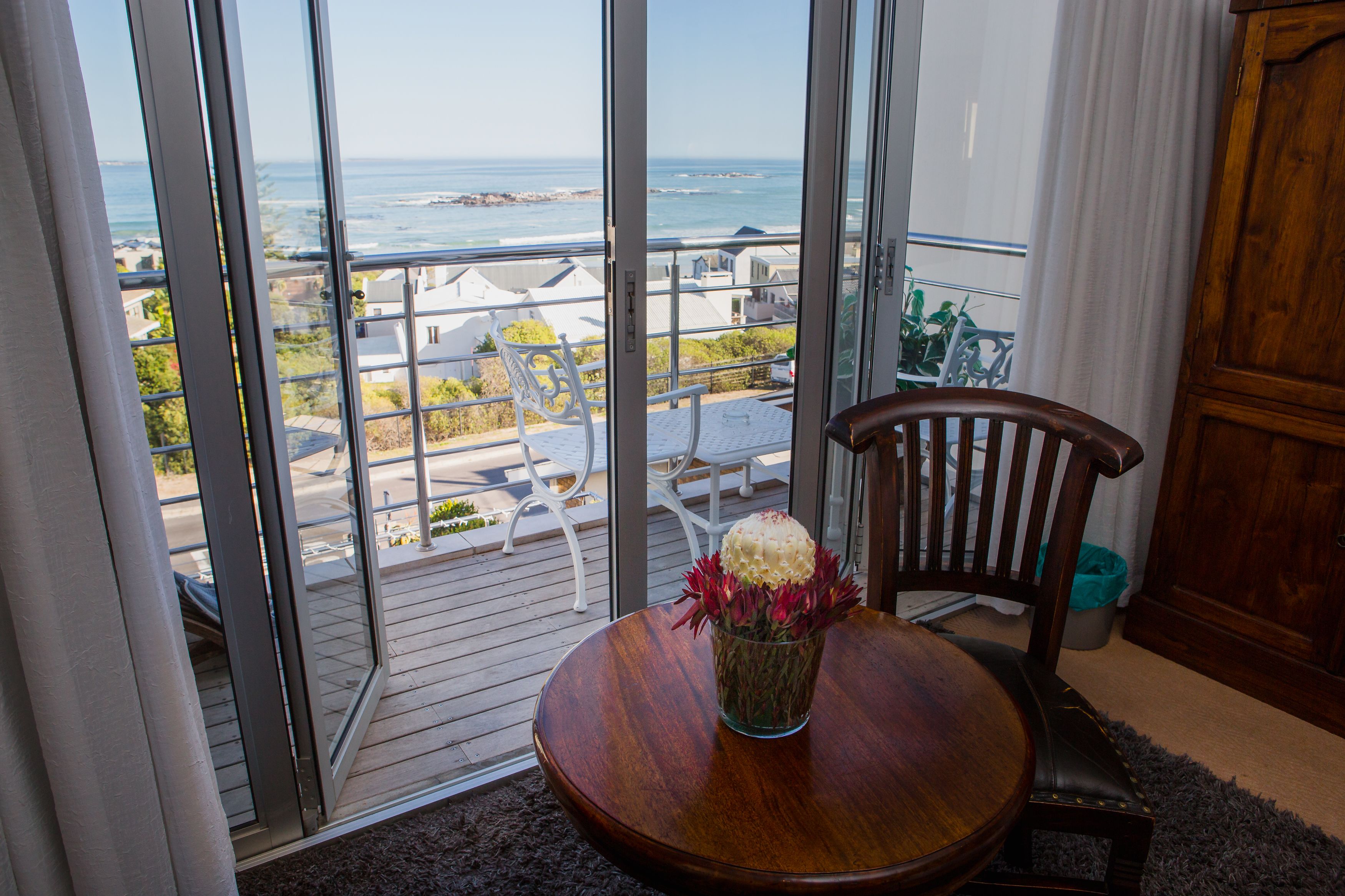 A room with a wooden table, a chair, and a view of the ocean through large glass doors.