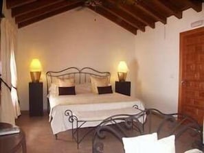 A bedroom with a bed, two bedside lamps, a wooden door, and a small table. - Hotel Palacio Blanco (Velez-Malaga)