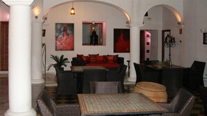 A spacious lobby with high ceilings, a central seating area with a sofa and chairs, and a large table. There are two arches framing the seating area, and artwork is displayed on the walls. - Hotel Palacio Blanco (Velez-Malaga)