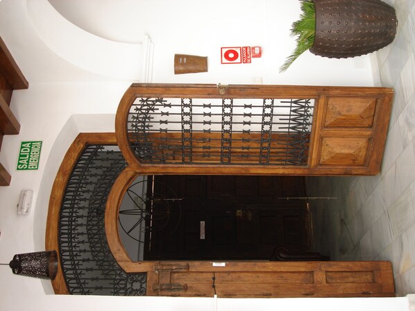 A room with a wooden cabinet, a black metal gate, and a red emergency exit sign. - Hotel Palacio Blanco (Velez-Malaga)