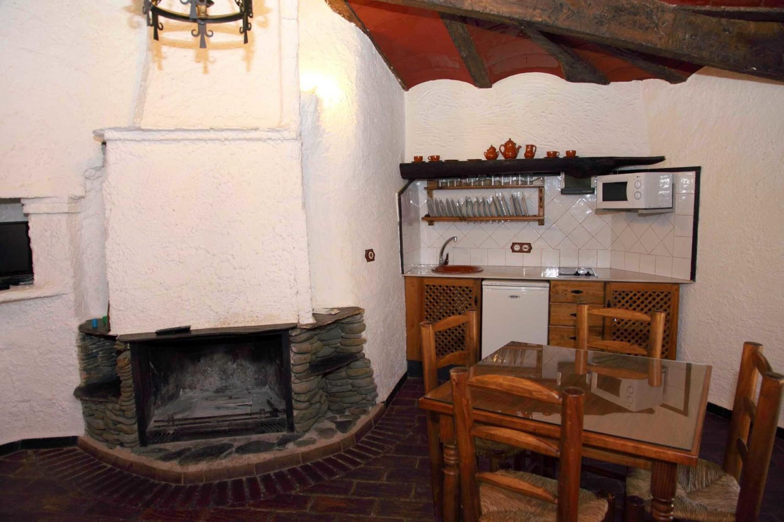 Una cocina rústica con chimenea de piedra, mesa de comedor de madera y un microondas sobre la encimera.