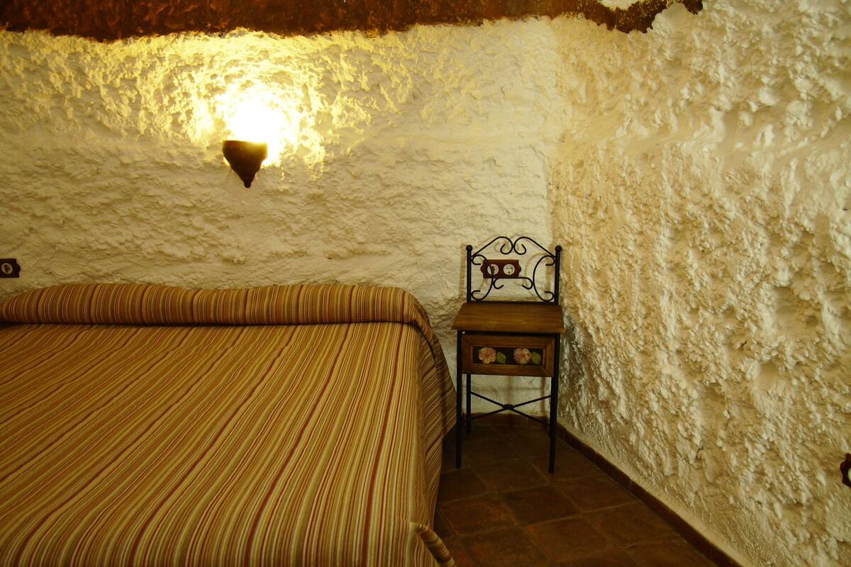 Ein Zimmer mit einem Bett, einem kleinen Tisch mit Stuhl und einer Wandleuchte.