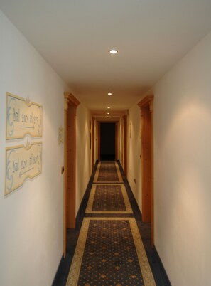 Un long couloir étroit, doté d’un tapis à motifs, de portes en bois et de panneaux indicateurs fixés au mur.