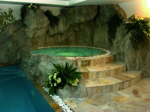 Una piscina interior con bañera de hidromasaje, escalones de piedra y paredes de roca circundantes.