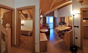 Een knus ingerichte kamer met een bed, een klein tafeltje en een bank. Er is een televisie en een lamp.