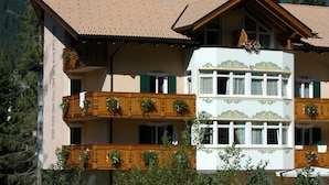 A multi-story building with balconies, a tiled roof, and a mountainous backdrop. - Residence Pez Gajard (Primiero San Martino di Castrozza)