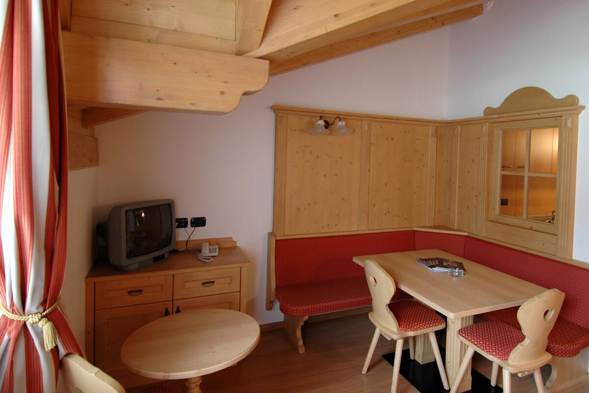 Interior de una cabaña de madera con una mesa, dos sillas, un televisor y un armario.