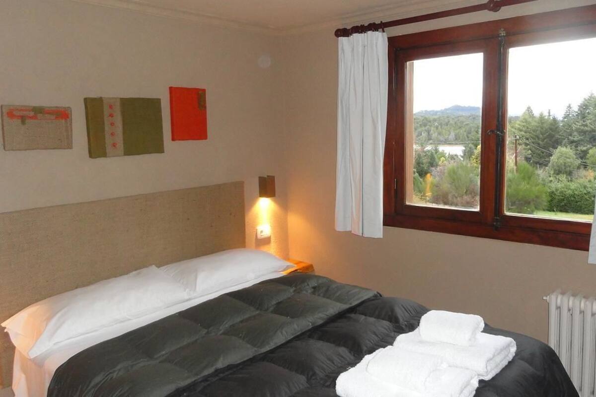 Une chambre à coucher avec un lit, une fenêtre avec des rideaux, un luminaire fixé au mur et un radiateur.